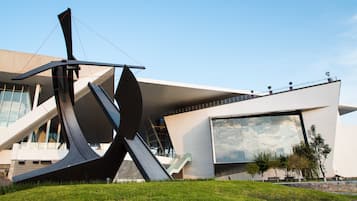 A modern building with a unique architectural design, featuring a prominent sculpture in the foreground and a large glass facade on the side.