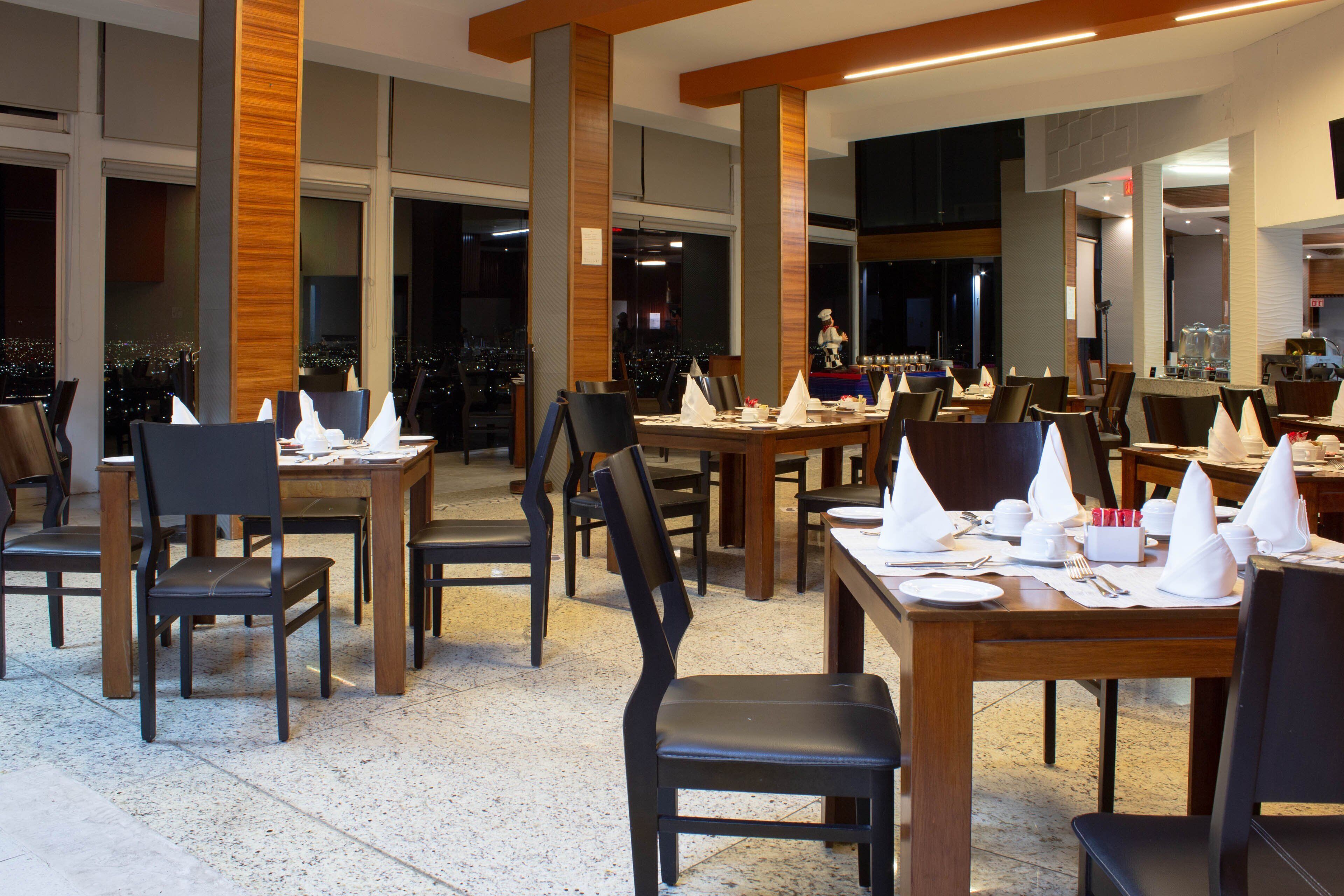 A restaurant with multiple tables and chairs, large windows, and a city view.