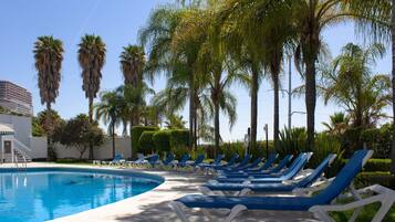 Un área de piscina con sillas de descanso y palmeras.