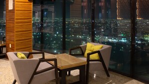 A modern room with a city view, featuring a sofa, a small table, and a wooden accent piece. - Holiday Inn Queretaro Zona Diamante by IHG (Querétaro)