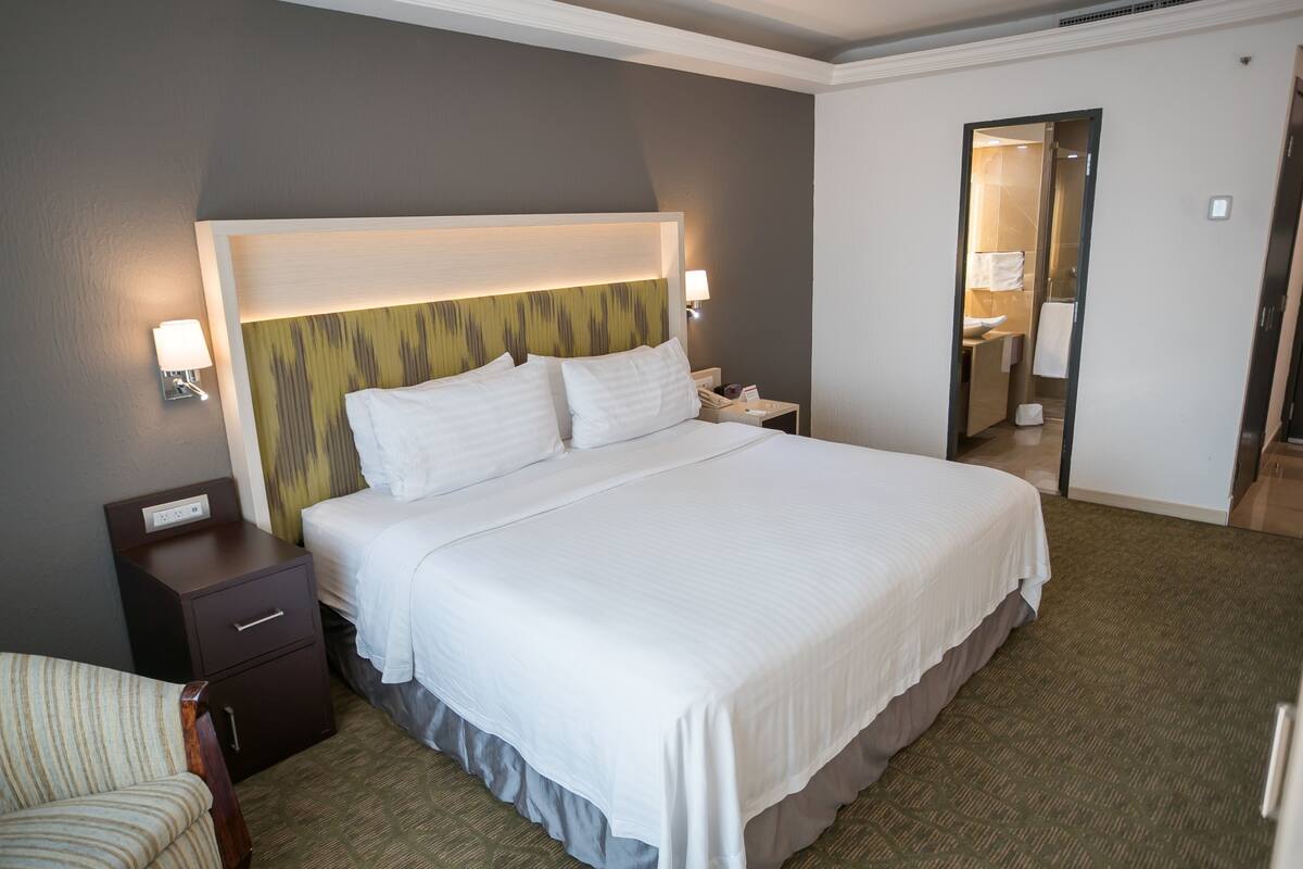 A hotel room with a large bed, a nightstand, a chair, and a bathroom visible through an open door.