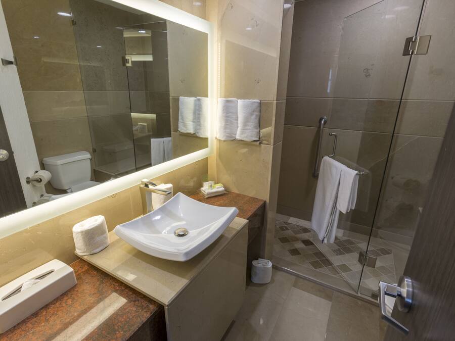 Un baño moderno con un espejo grande, un lavamanos, un inodoro y una cabina de ducha de vidrio.