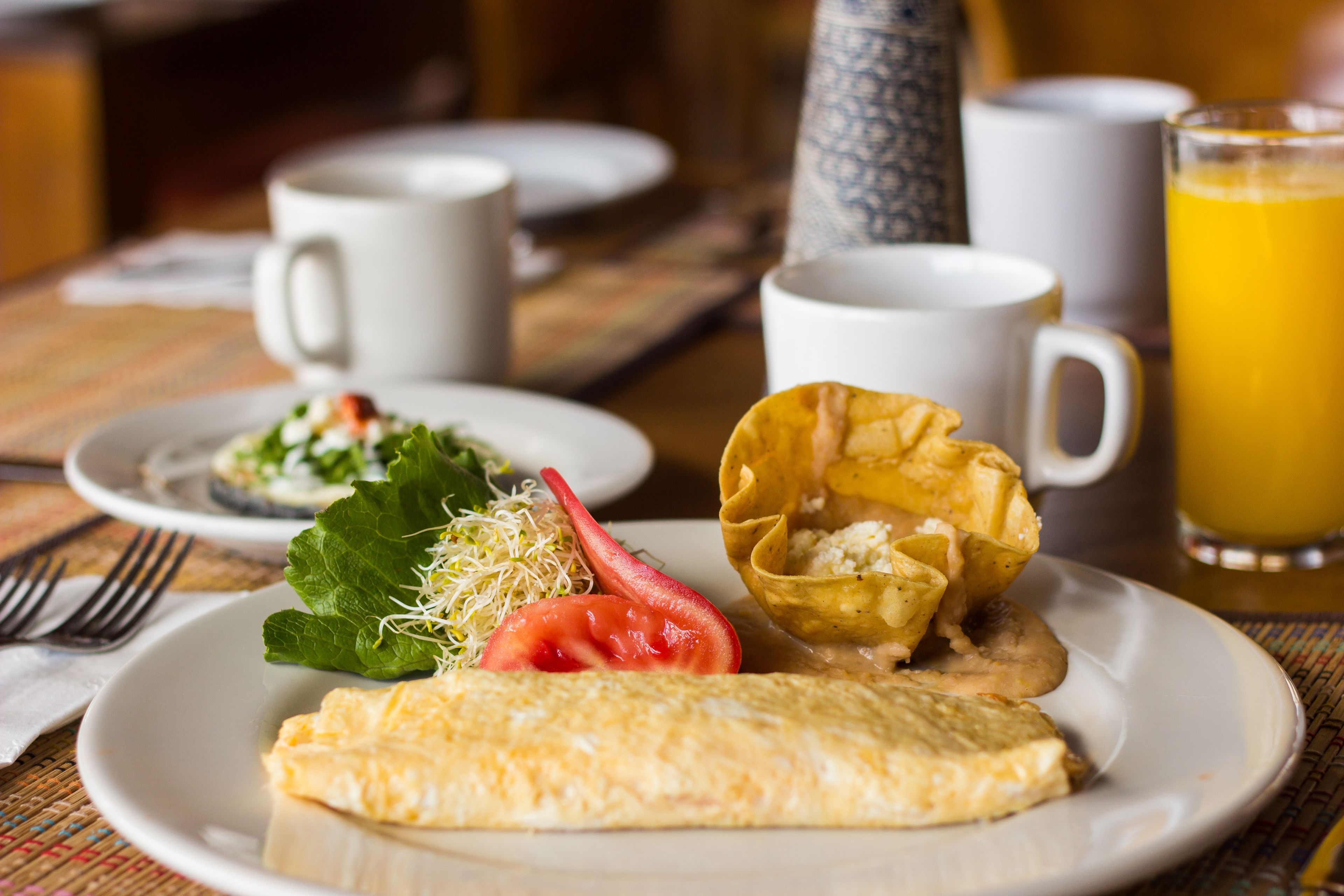 Un desayuno con un plato de comida, una taza de café y un vaso de zumo de naranja.