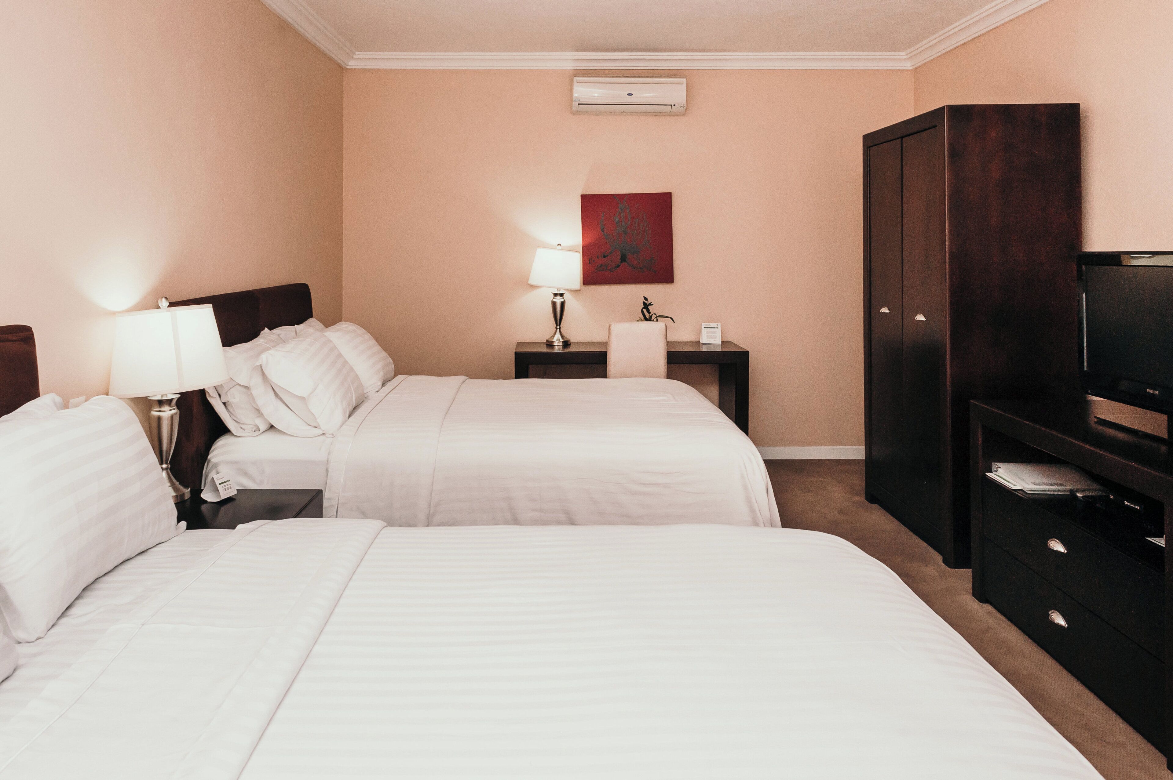 Une chambre d’hôtel avec deux lits, un bureau avec une lampe, une télévision et une armoire.