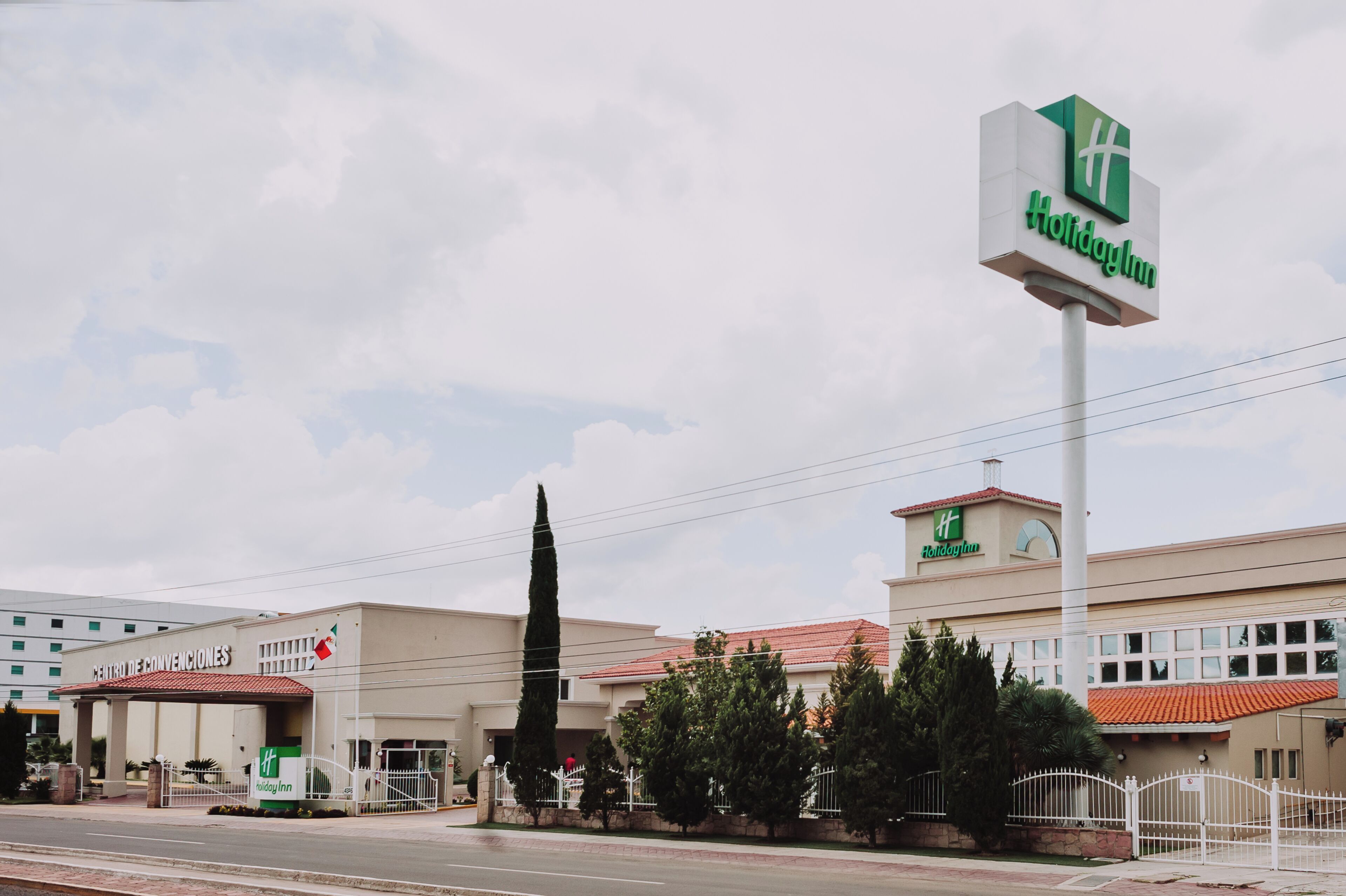 Un hotel Holiday Inn con un letrero llamativo, un estacionamiento y un edificio con techo de tejas rojas.