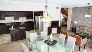 A modern kitchen with dark cabinets, a stainless steel refrigerator, and a dining area with a glass table and wicker chairs.