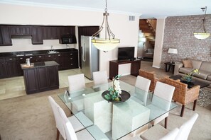 A modern kitchen with dark cabinets, a stainless steel refrigerator, and a dining area with a glass table and wicker chairs.