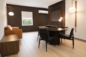 A modern living room with a sofa, a dining table with chairs, a wooden coffee table, and a built-in TV.