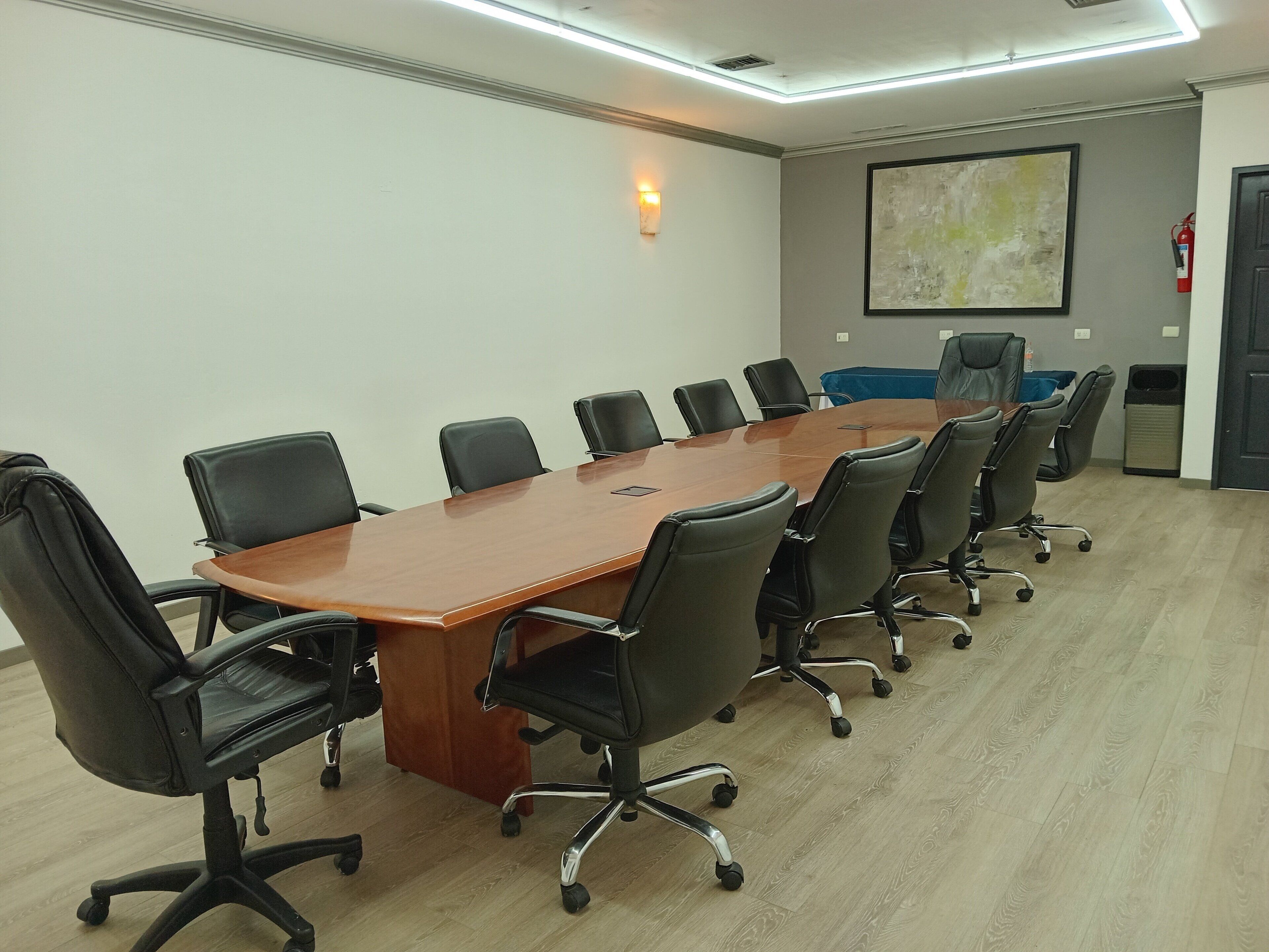A conference room with a long wooden table surrounded by black office chairs, a whiteboard, and a fire extinguisher.
