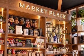 Un puesto de mercado con un letrero que dice 'MARKET PLACE' y estantes llenos de diversos artículos, incluyendo bocadillos, tazas y botellas.