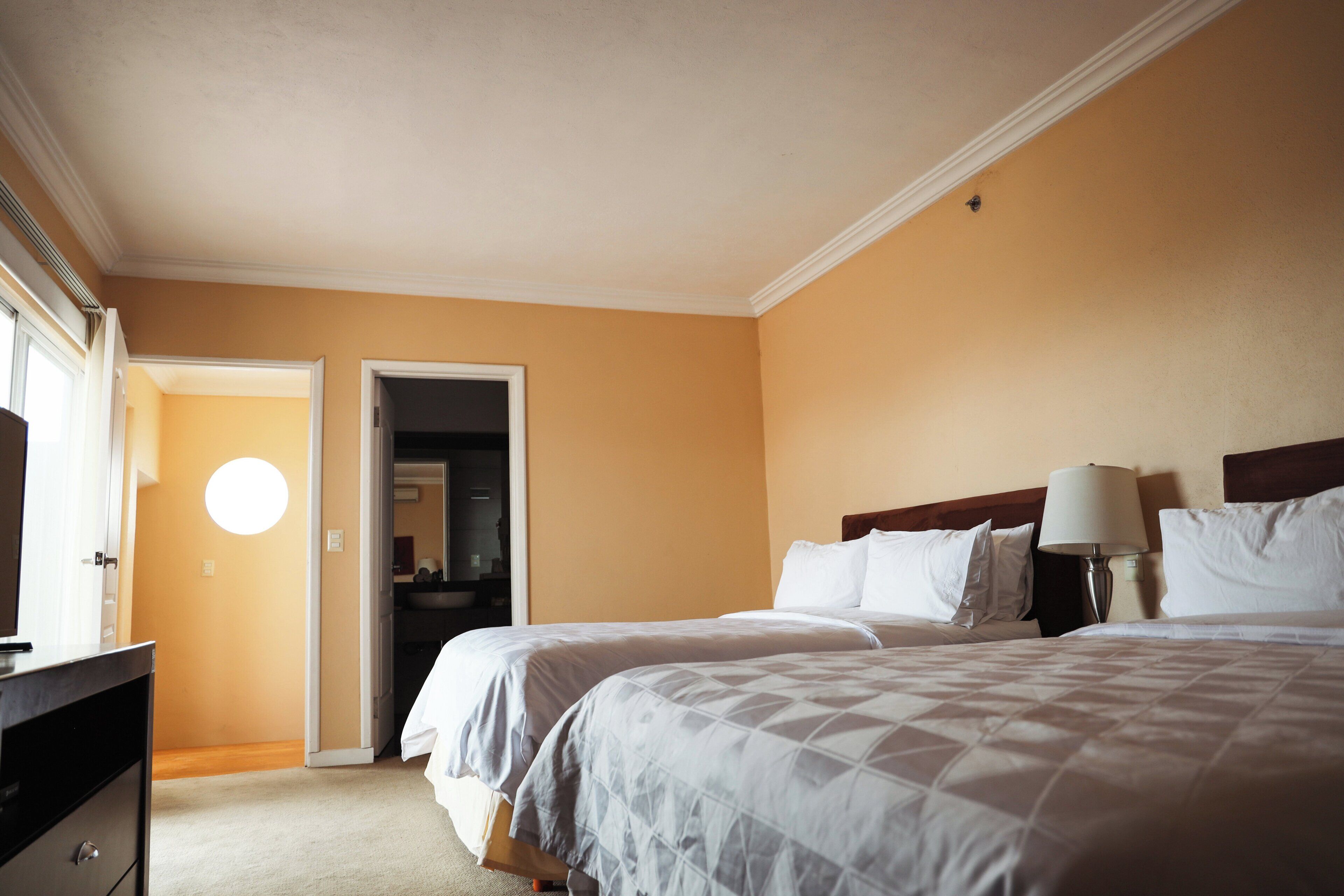 Een hotelkamer met twee bedden, een dressoir, een lamp en een deur naar de badkamer.