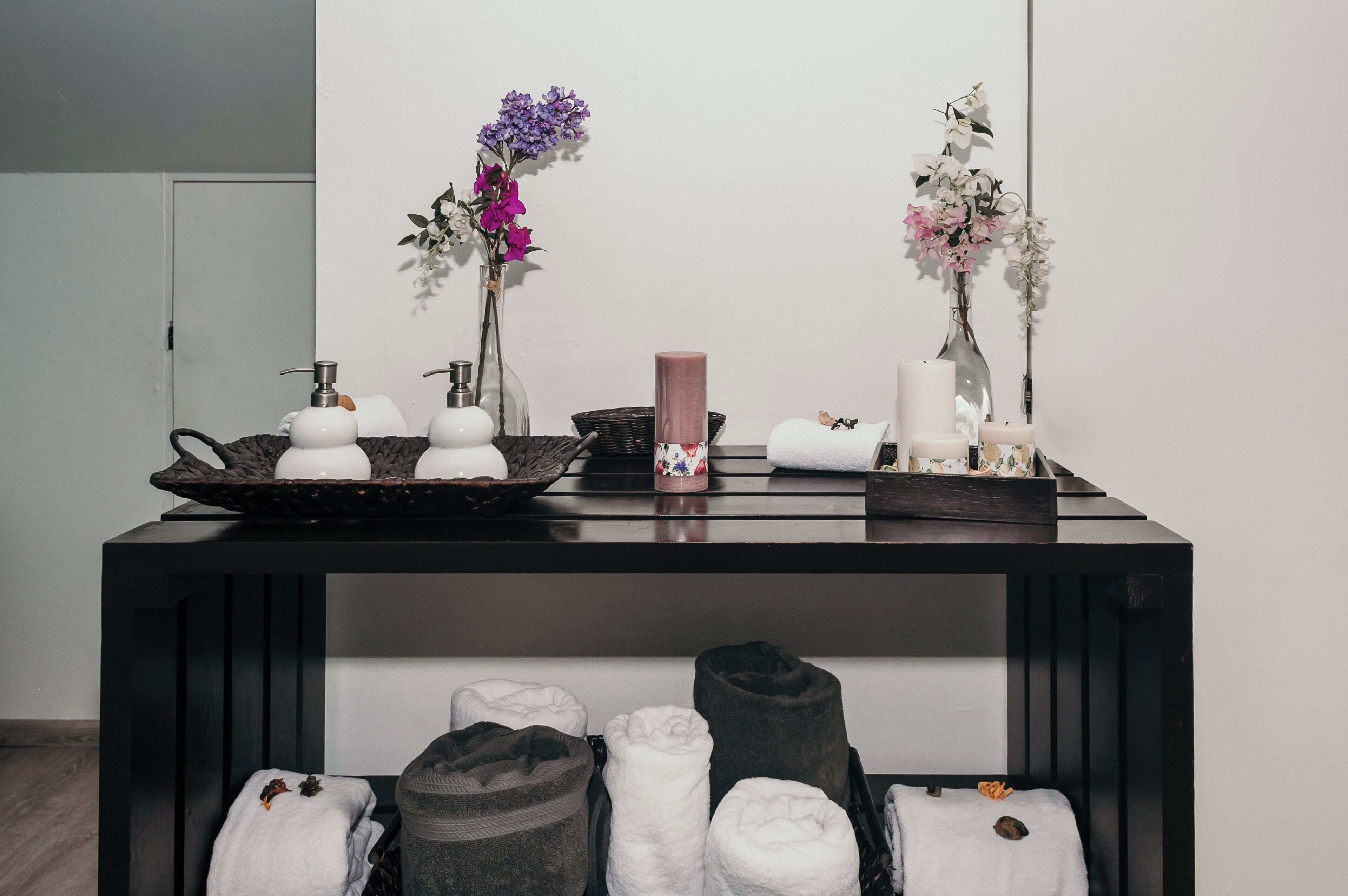 A bathroom vanity with a black countertop, a mirror, and a shelf below holding towels and a candle.