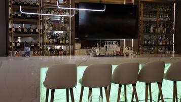 Una zona de bar con una gran pantalla de televisión, estantes con botellas de licor y taburetes.