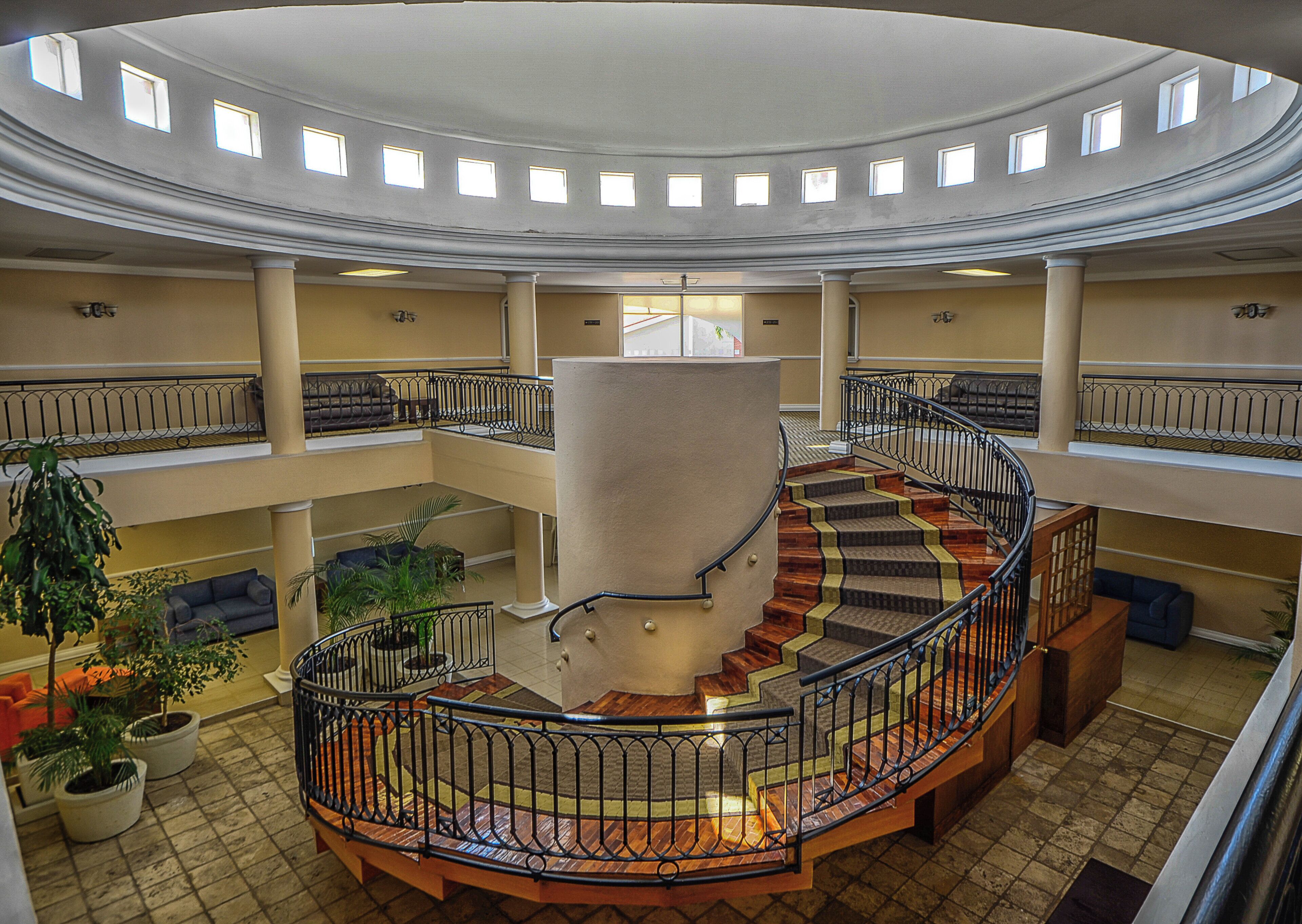 A multi-level atrium with a central spiral staircase, multiple balconies, and potted plants.