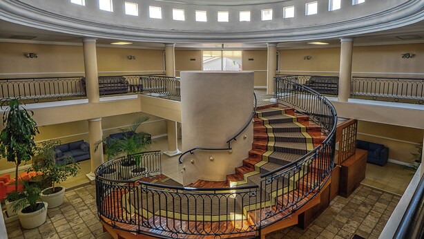 A multi-level atrium with a central spiral staircase, multiple balconies, and potted plants.