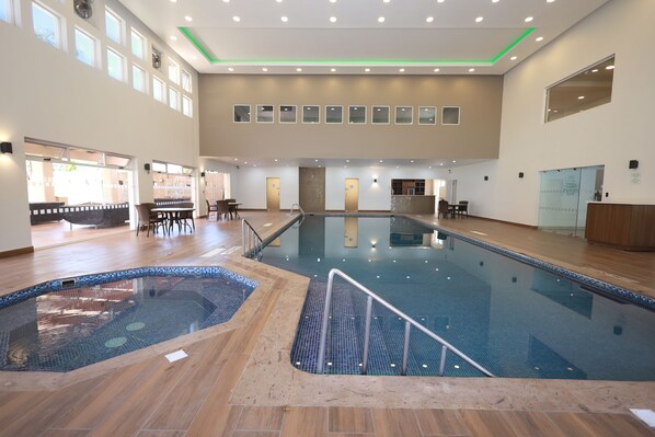 An indoor swimming pool with a tiled floor, a small hot tub, and a reception area with a counter and chairs. - Holiday Inn Durango by IHG (Durango)