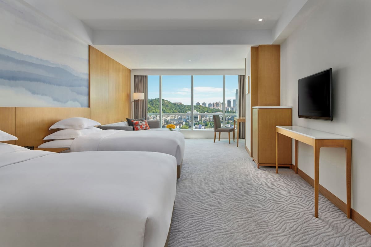 Ein Hotelzimmer mit zwei Betten, einem Fernseher, einem Schreibtisch und Blick auf die Stadt.