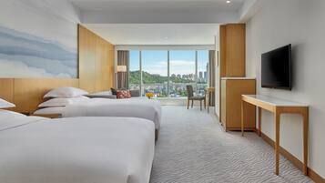 Habitación de hotel con dos camas, televisión, escritorio y vista a la ciudad.