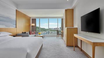 Una habitación de hotel moderna con una cama grande, un escritorio, un televisor de pantalla plana y vistas a la ciudad a través de amplios ventanales.