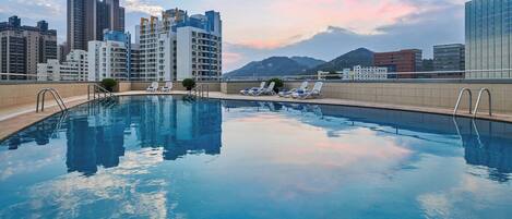 A swimming pool with lounge chairs and a cityscape in the background.