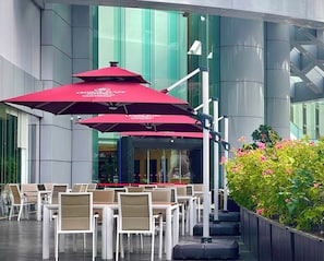 Outdoor seating with umbrellas, a modern building facade, and a planter with flowers. - Crowne Plaza Zhuhai City Center by IHG (Zhuhai)