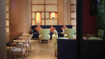 A modern lounge area with a wooden panel wall, a blue sofa with orange cushions, and several light-colored armchairs.