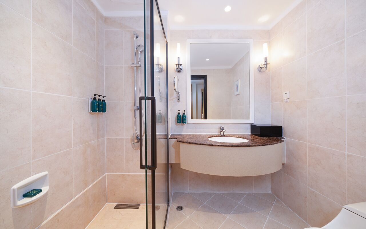 A modern bathroom with a glass-enclosed shower, a round sink with a marble countertop, and beige tiles.