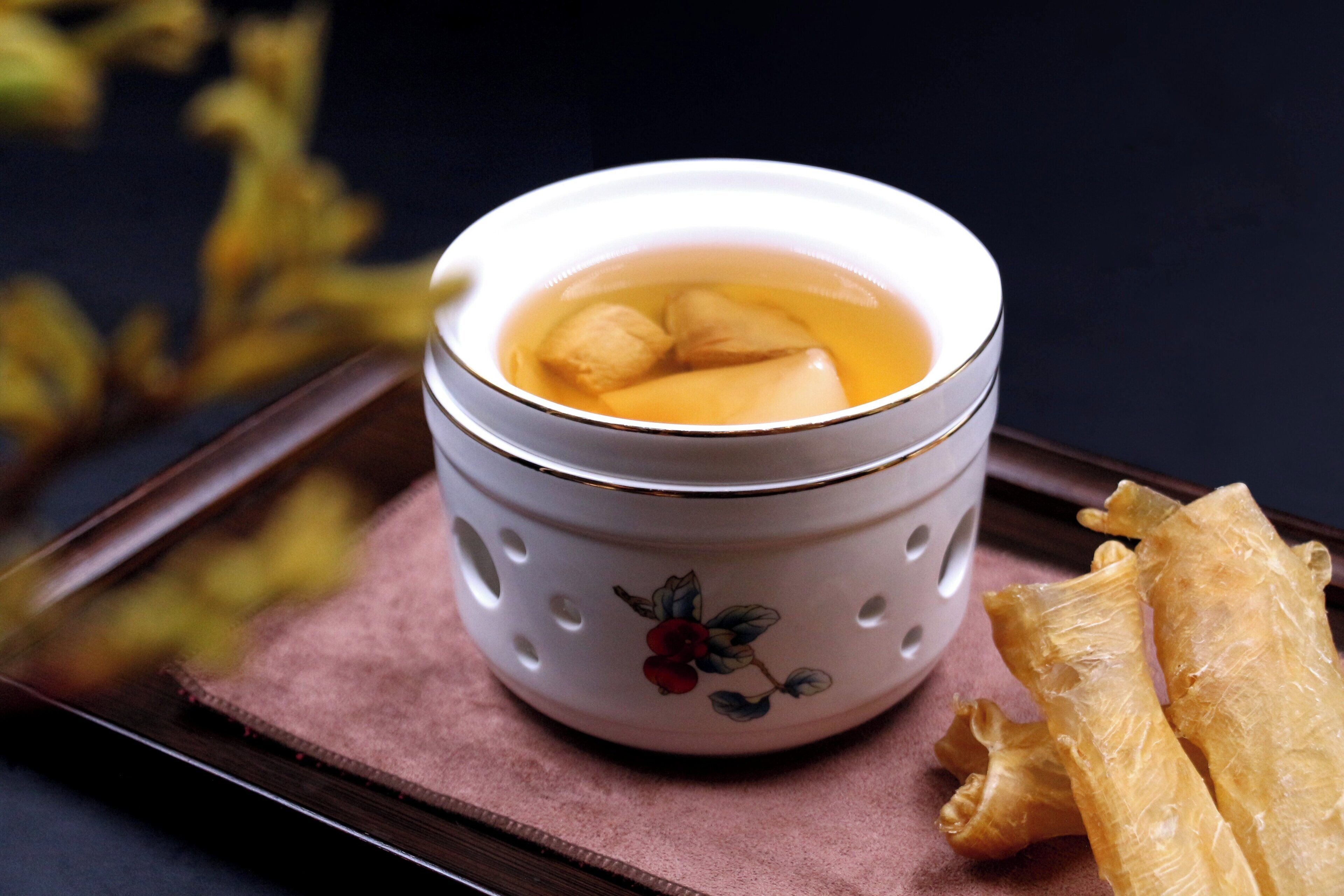 A ceramic cup with a floral design, filled with a clear liquid and two round objects, placed on a tray with a pink cloth.