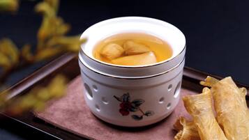 A ceramic cup with a floral design, filled with a clear liquid and two round objects, placed on a tray with a pink cloth.