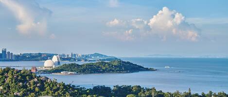 A coastal cityscape with a prominent white dome structure, dense greenery, and a clear view of the sea.