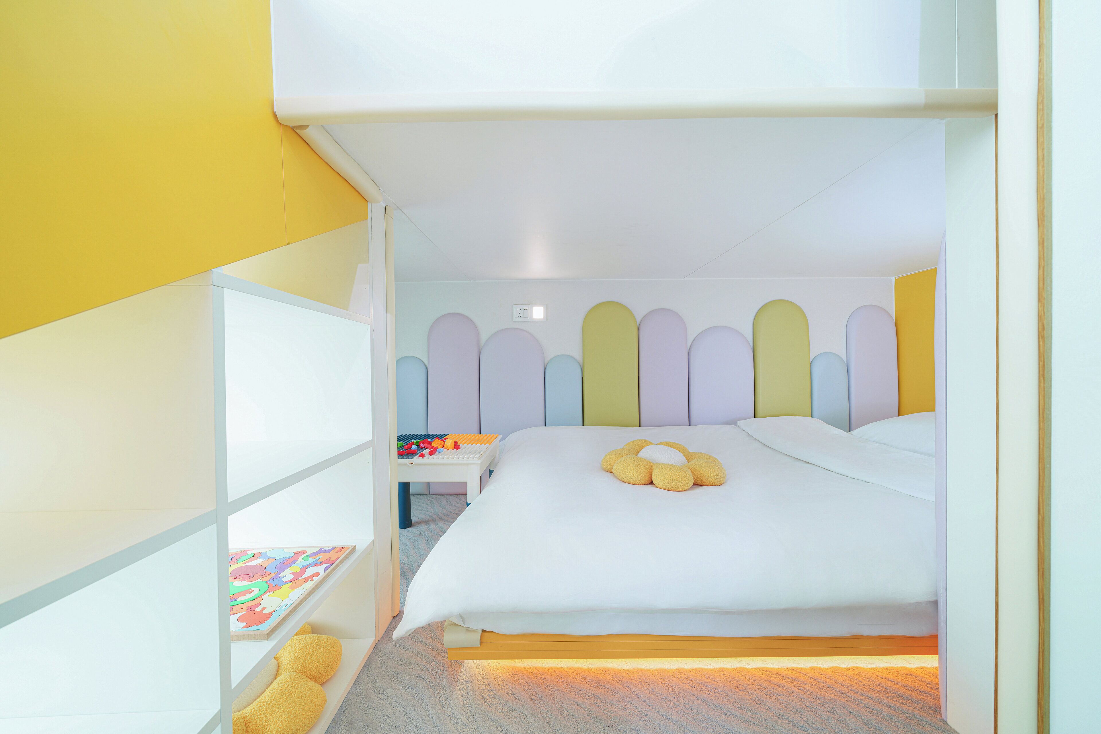 A compact room with a bed, a small table with toys, and a shelf with books.