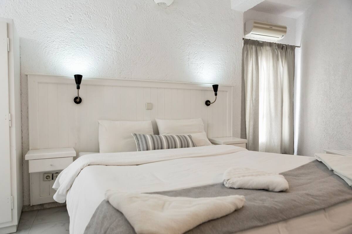 A neatly arranged bedroom with a large bed, bedside tables, and a wall-mounted air conditioning unit.