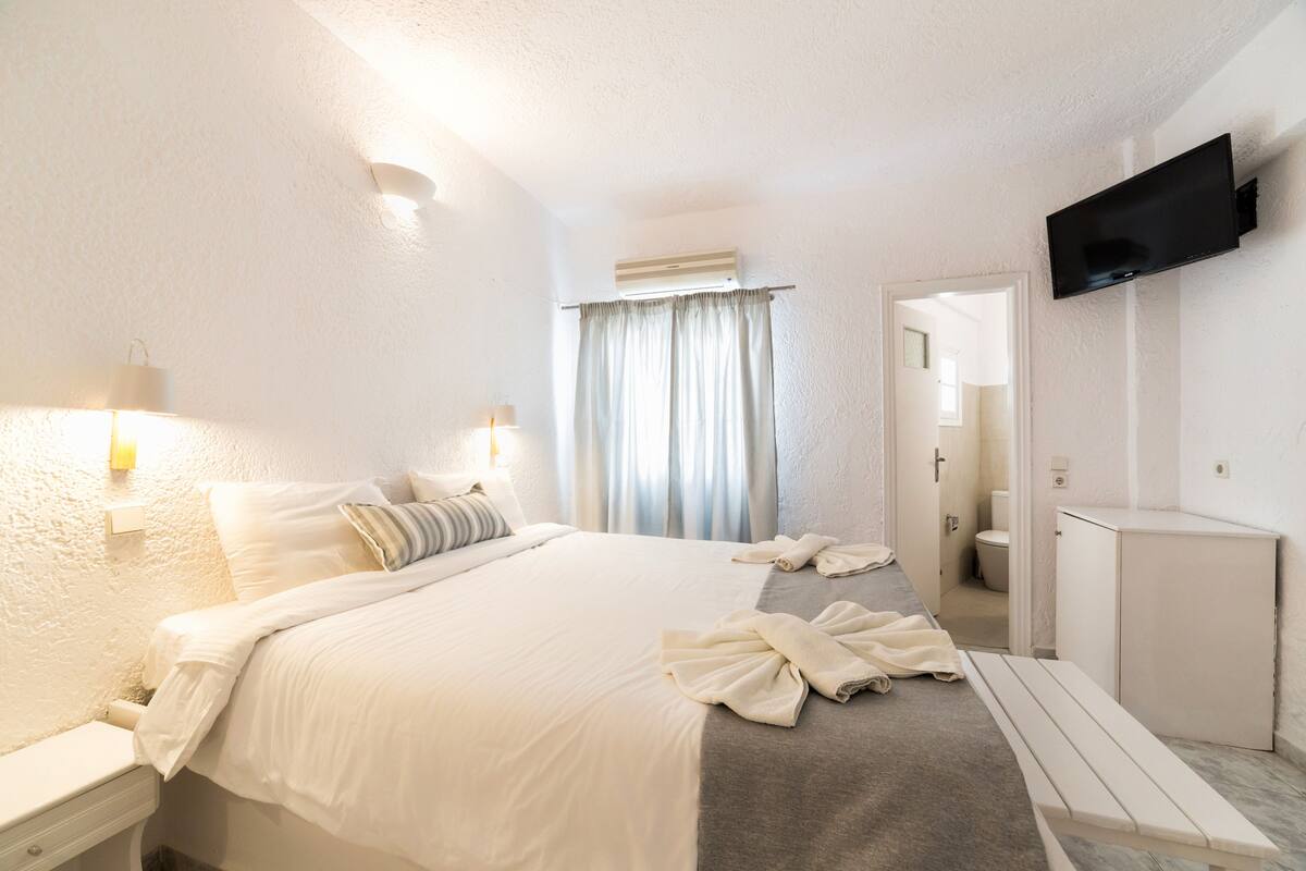 A hotel room with a bed, bedside table, and a TV mounted on the wall.