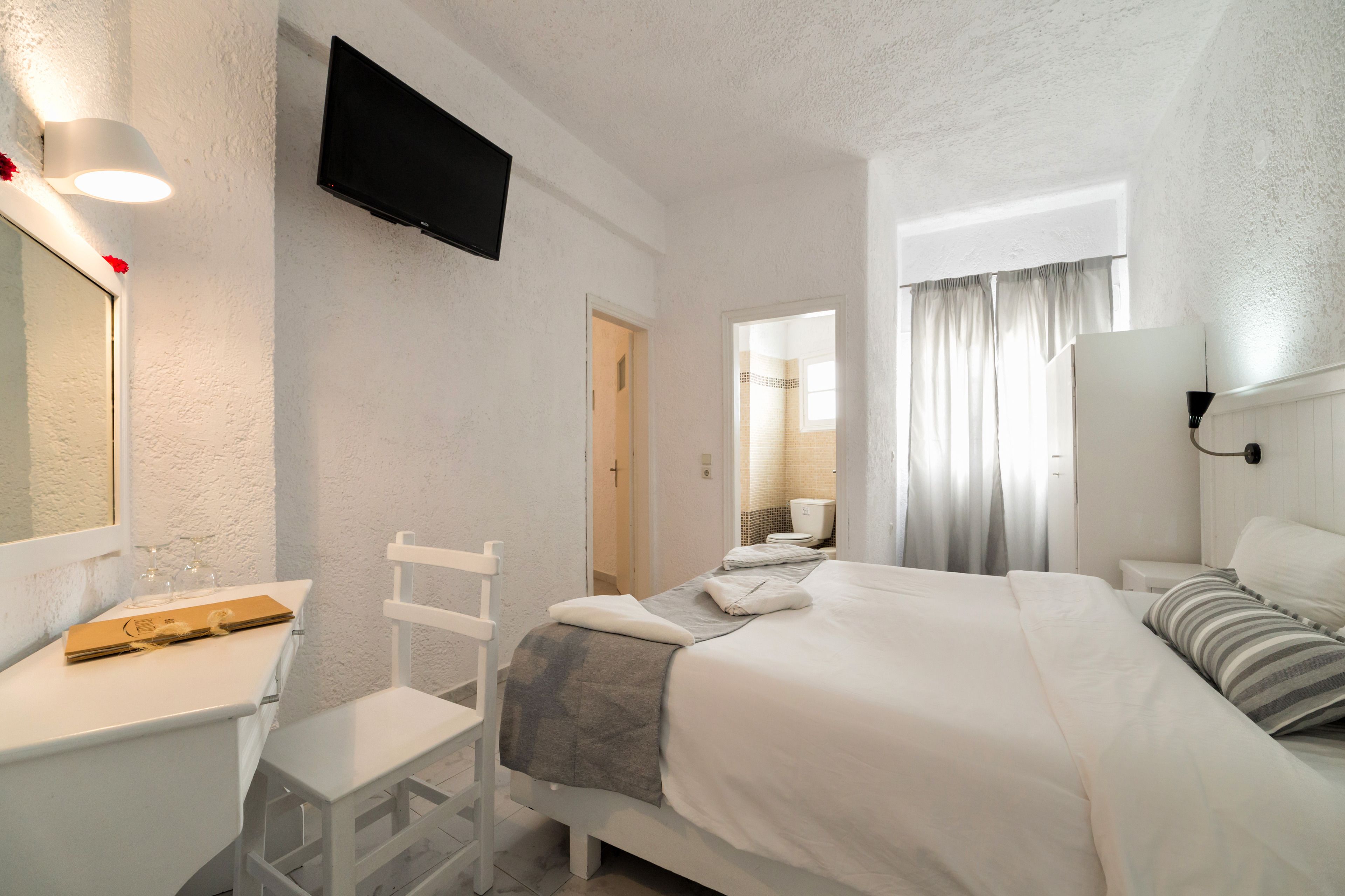 Une chambre d’hôtel équipée d’un lit, d’un bureau, d’une chaise, d’une télévision et d’une fenêtre avec des rideaux.