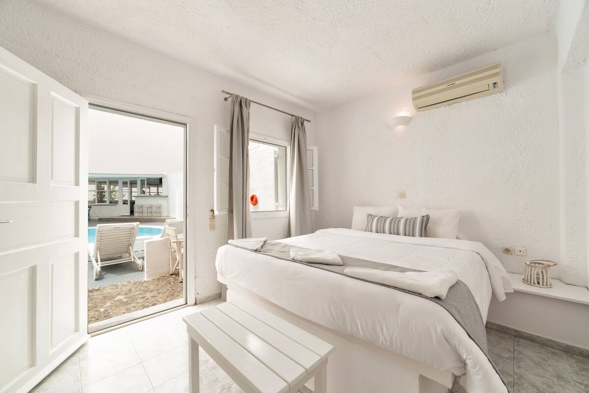 A bedroom with a bed, bedside table, and a view of a pool area.