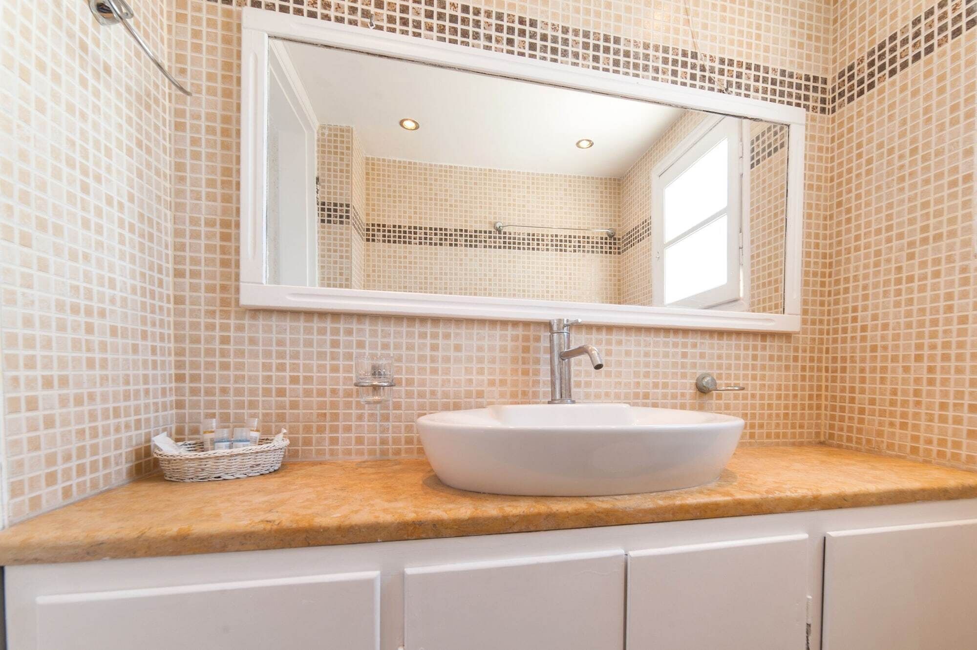 Baño con lavamanos blanco, espejo y pared de azulejos.