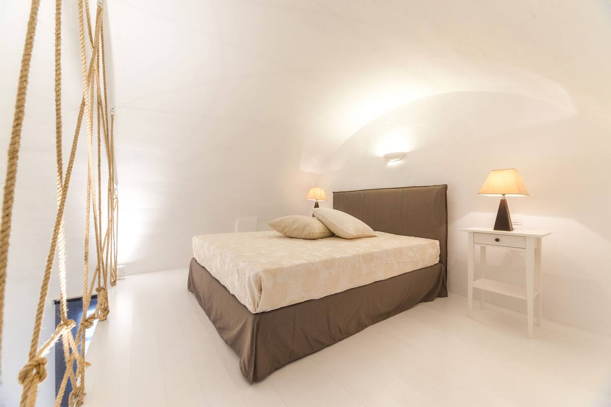 A bedroom with a bed, bedside lamps, and a small nightstand.
