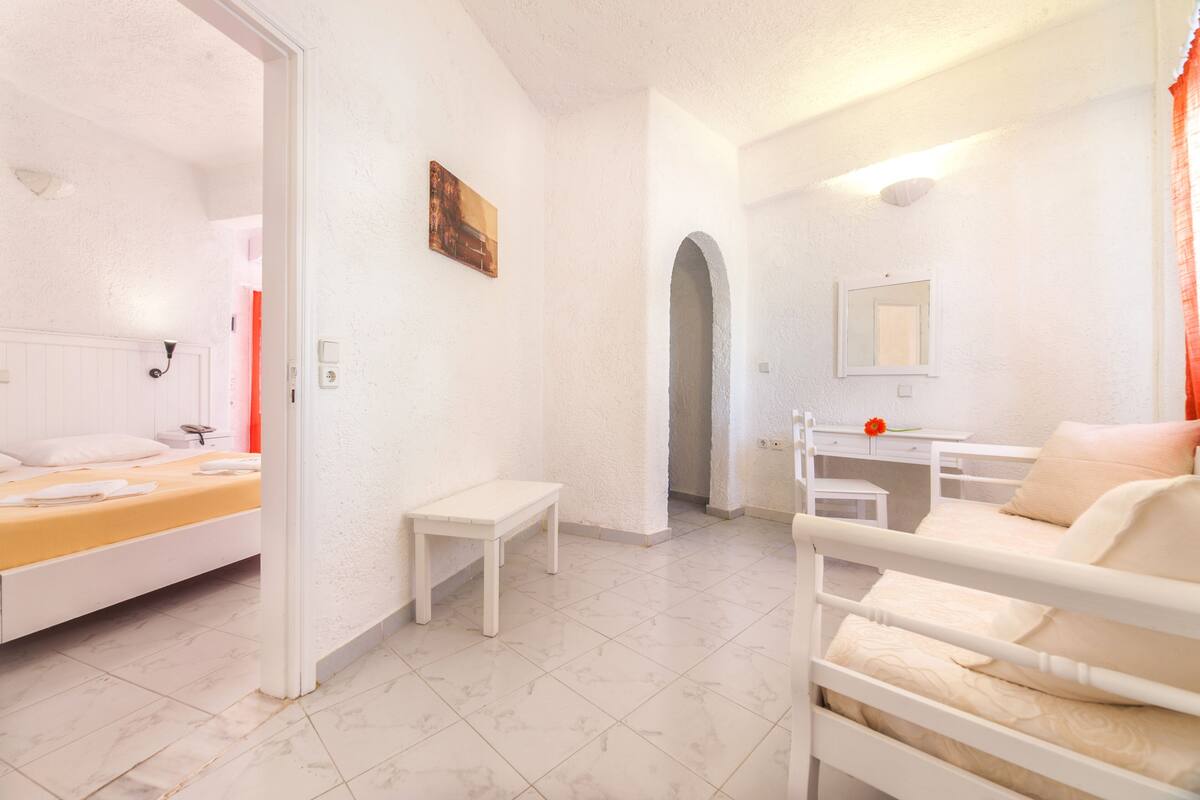 A room with a bed, a desk, a mirror, and a small table.