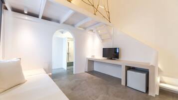 A modern, white-themed loft bedroom with a built-in TV, a small fridge, and a cozy seating area.