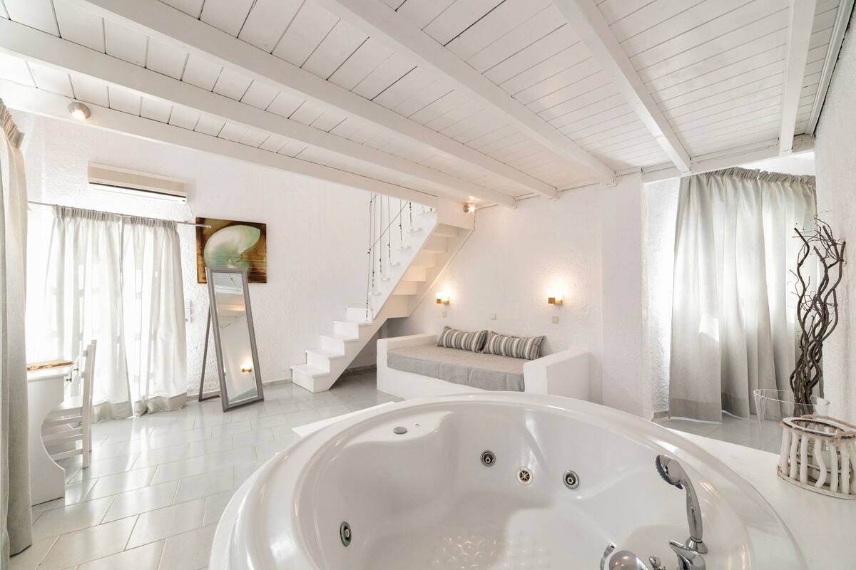 A modern bathroom with a large bathtub, white walls, and a staircase leading to a seating area.