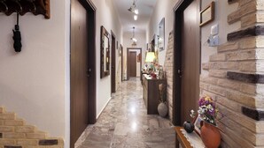 A hallway with a marble floor, wooden doors, and a brick accent wall. There is a bench with a vase of flowers and a picture frame. - Mpalkoni Sti Monemvasia (Monemvasia)