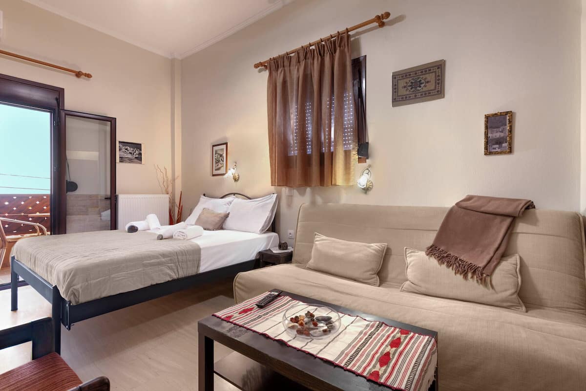 Un dormitorio con cama, sofá, mesita de noche y ventana con cortinas.