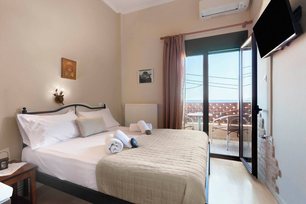 Habitación de hotel con cama, mesita de noche, televisor montado en la pared y balcón con vistas.