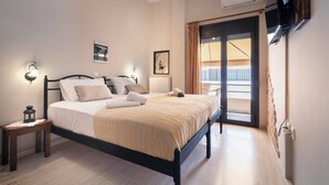 A bedroom with a bed, bedside tables, wall-mounted TV, and a view of the outside balcony. - Mpalkoni Sti Monemvasia (Monemvasia)