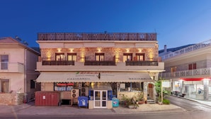A two-story building with a stone facade, a balcony with metal railings, and a storefront with signage. - Mpalkoni Sti Monemvasia (Monemvasia)