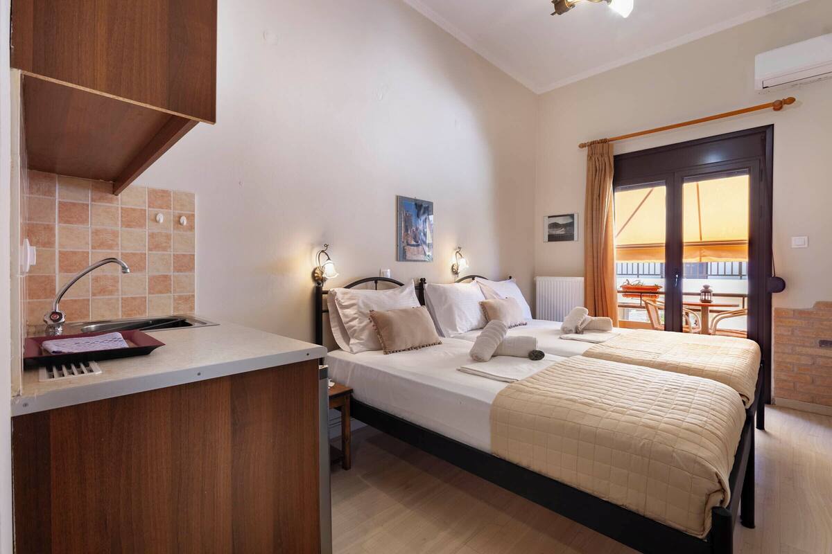 Un dormitorio con dos camas, una kitchenette pequeña, una ventana con cortinas y vistas al exterior.