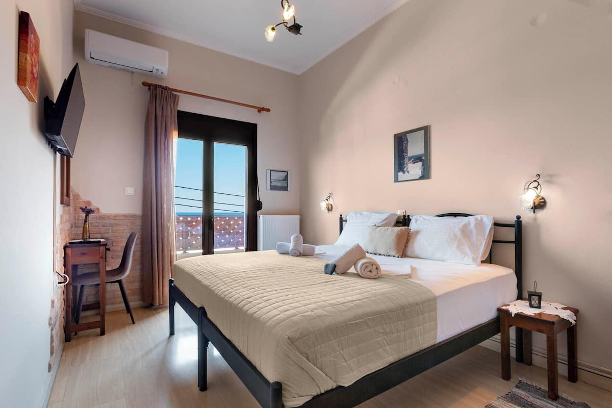 Un dormitorio con cama, escritorio, silla, una mesita y puerta al balcón.