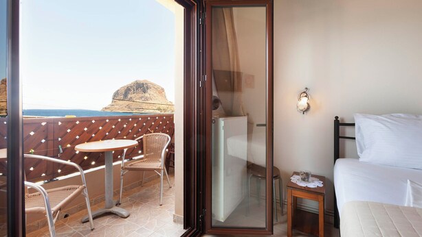 A balcony with wicker chairs, a small table, a bed, and a view of a mountain. - Mpalkoni Sti Monemvasia (Monemvasia)