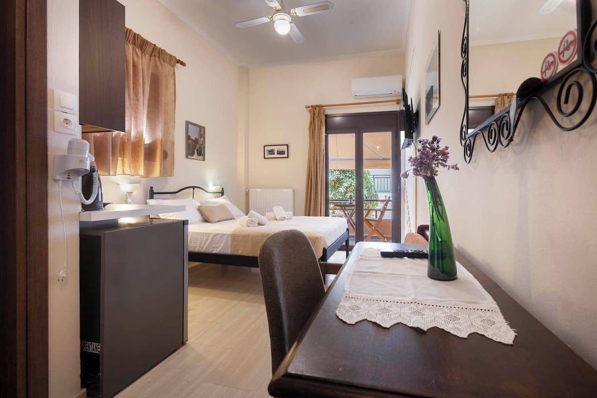 Un dormitorio con cama, escritorio, silla, una mesa con un florero y un balcón con vistas.
