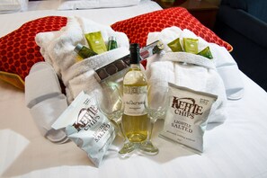 A bed with a bottle of Valetordor white wine, a bag of Kettle Chips, and a bag of lightly salted snacks.